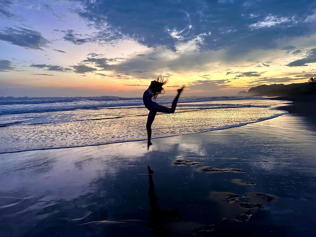 A dancer silhouetted against a colorful Central Pacific sunset reflected on the shoreline