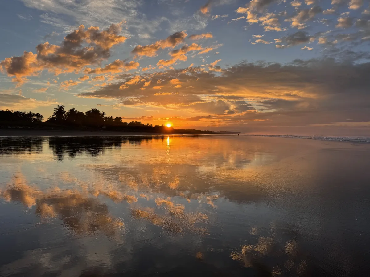Golden sunrise clouds mirrored in the calm shoreline at Playa Hermosa