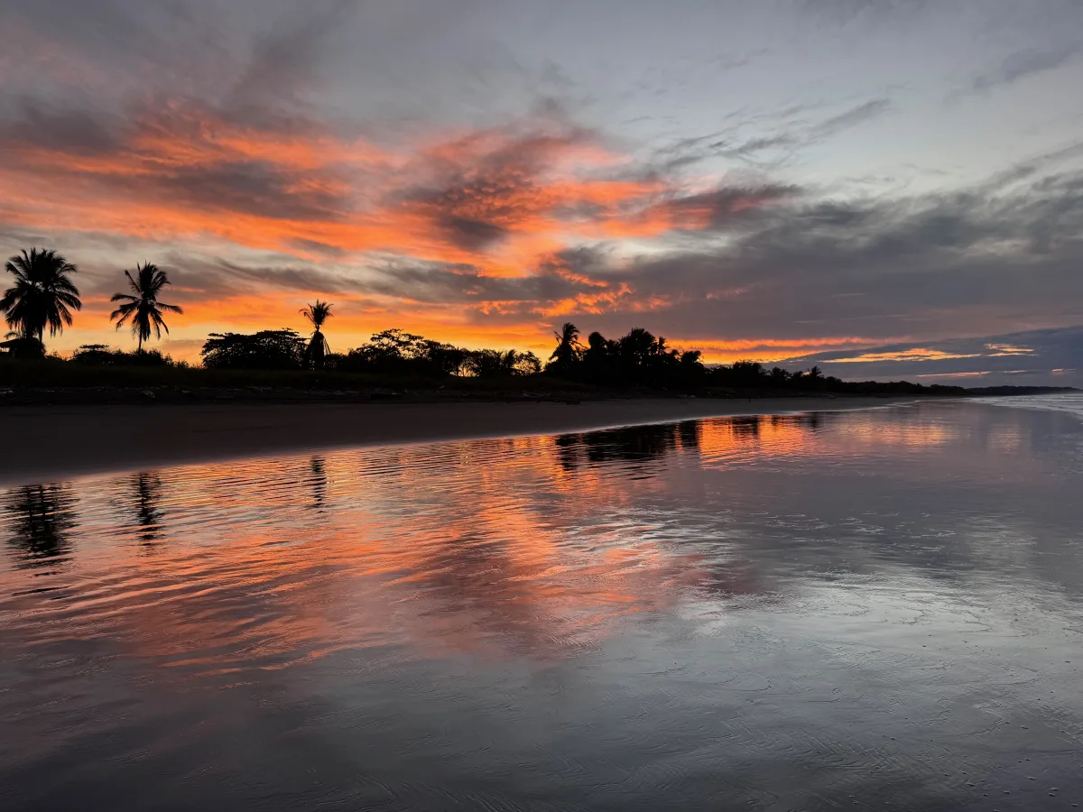 A fiery red sunrise reflected across the wet sand at Playa Hermosa, Costa Rica