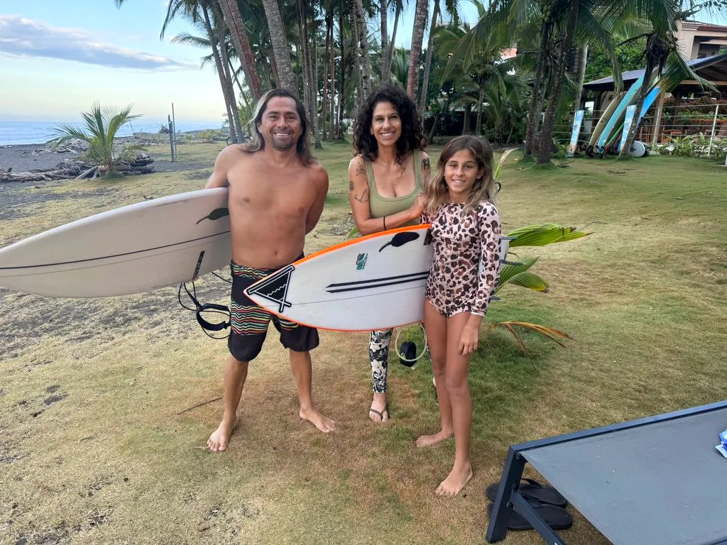 Álvaro Solano, YoYo and her daughter Lani holding surfboards beside Playa Hermosa